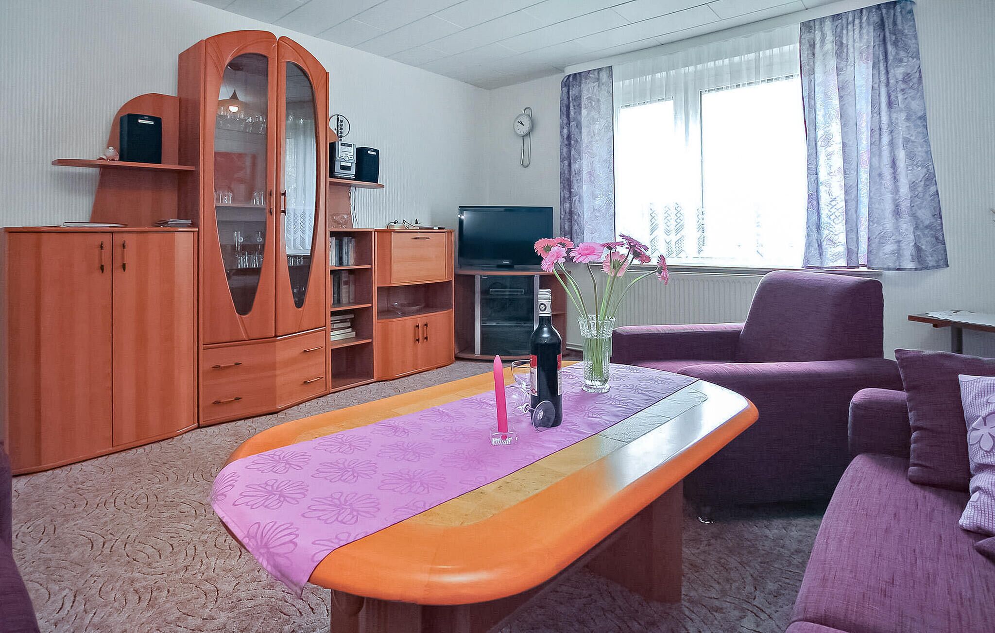 Un salon comprenant un meuble en bois, un téléviseur, un canapé et une table basse sur laquelle est posé un vase de fleurs.