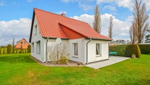 Ett envåningshus med ett rött tegeltak, vita fasadväggar och en liten trädgård framför huset, med en häck och en krukväxt.