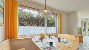 A dining area with a wooden table set for four, a window with a view of trees, and a hanging light fixture. - Ferienwohnung Pruchten (Pruchten)