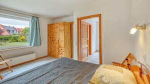 A bedroom with a bed, a wooden wardrobe, a window with a curtain, and a view of a garden. - Ferienwohnung Pruchten (Pruchten)