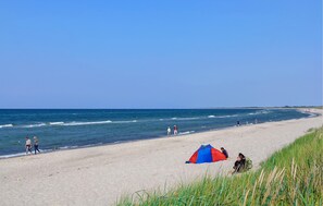 Een strand met heldere lucht, golven en mensen die wandelen.