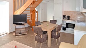 Un soggiorno moderno con scala in legno, zona pranzo con tavolo e sedie, televisore su un mobile e angolo cottura con macchina del caffè.