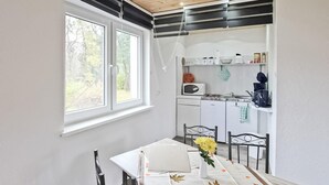 Cocina compacta con armarios blancos, microondas y pileta. Hay una mesa de comedor con sillas y un florero.