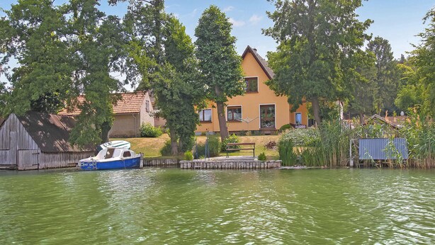 Una casa al costat d'un llac tranquil amb una barca amarrada a prop.