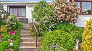 Un jardin résidentiel agrémenté d’un escalier en pierre menant à une porte, le tout entouré de diverses plantes et arbustes en fleurs.