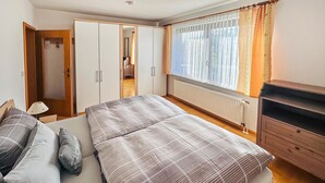 Une chambre à coucher avec un lit, une armoire, un radiateur et une fenêtre avec des rideaux.