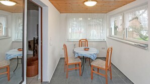 Ein Essbereich mit Tisch und vier Stühlen, einem Fenster mit Vorhängen und einer Holzbalkendecke.