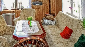 Una sala de estar acogedora, con piso de madera, un sofá estampado, una mesa de comedor con mantel de encaje y una silla de mimbre.