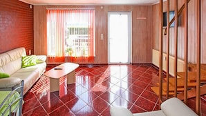 A living room with a sofa, a coffee table, and a chair. There is a door leading outside and a window with curtains.