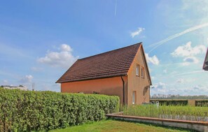 Eenlaags huis met schuin dak, omgeven door een verzorgde haag en een veld met hoog gras.