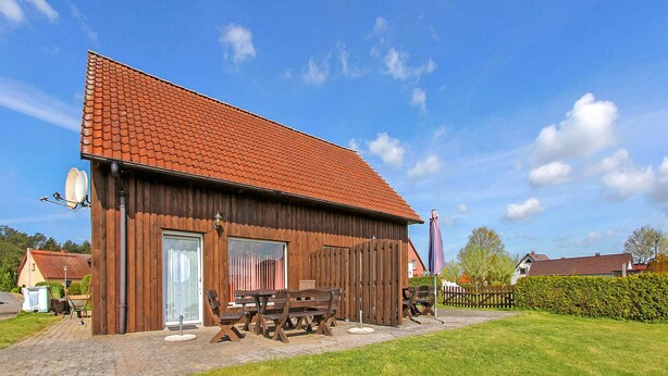 A wooden barn-style building with a red-tiled roof, a large door, and a patio area with wooden benches.