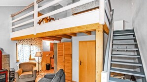 Een loft-achtige kamer met een houten trap, een bank, een stoel en een lamp.