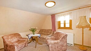 A small, cozy room with two plush armchairs, a small table with a vase of flowers, a radiator, and a lamp. - Ferienwohnung Neuhausen (Neuhausen/Erzgeb.)