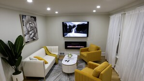 Un salon moderne avec un canapé blanc, des fauteuils jaunes, un téléviseur à écran plat et une cheminée.