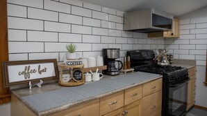 Une cuisine avec un dosseret de carreaux blancs, des armoires en bois, un coin café aménagé et une cuisinière.