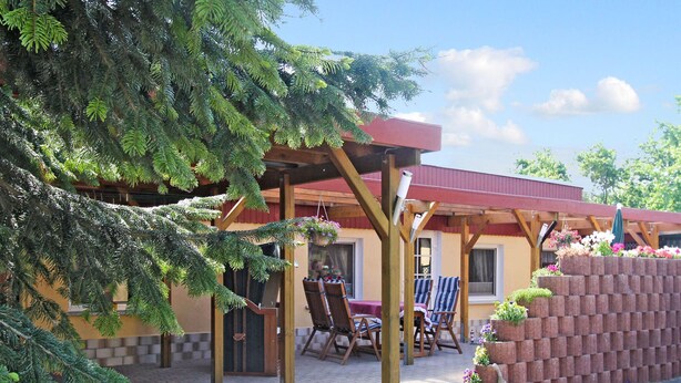 Un patio couvert avec un mur en briques, des chaises en bois et une table.