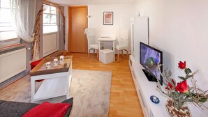 Un espace de vie compact comprenant un canapé, une table basse, un téléviseur et un petit coin repas avec des chaises.