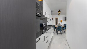 Une cuisine moderne avec des armoires blanches, un comptoir noir et une hotte de cuisine Bosch. On y trouve un coin repas avec une table dressée pour deux personnes, agrémentée de chaises colorées.