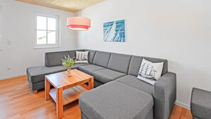 A modern living room with a grey sectional sofa, a wooden coffee table, and a small side table. There is a window with a view of the outside, a pink pendant light, and two wall-mounted paintings. - Gorgeous home in Ueckermünde (Seebad) (Ueckermünde (Seebad))