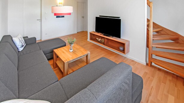 A modern living room with a grey sofa, a wooden coffee table, a flat-screen TV on a wooden stand, and a wooden staircase. - Gorgeous home in Ueckermünde (Seebad) (Ueckermünde (Seebad))