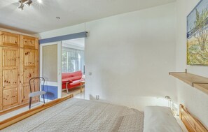 Une chambre à coucher avec un lit, une armoire en bois et un canapé rouge dans la pièce adjacente.