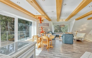 Une cuisine moderne avec une grande fenêtre, un coin repas avec des chaises en bois, un canapé et une vue sur les arbres.