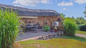 A rustic stone building with a thatched roof, a brick patio, and a stone wall. - Ferienwohnung Meesiger (Meesiger)
