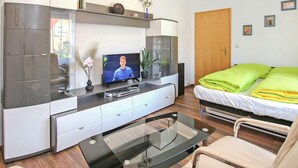 A modern hotel room with a flat-screen TV, a glass coffee table, a bed with green and yellow bedding, and a wooden door. - Ferienwohnung Meesiger (Meesiger)