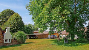 A residential area with a brick house, a garage, and a large tree providing shade. - Ferienwohnung Meesiger (Meesiger)