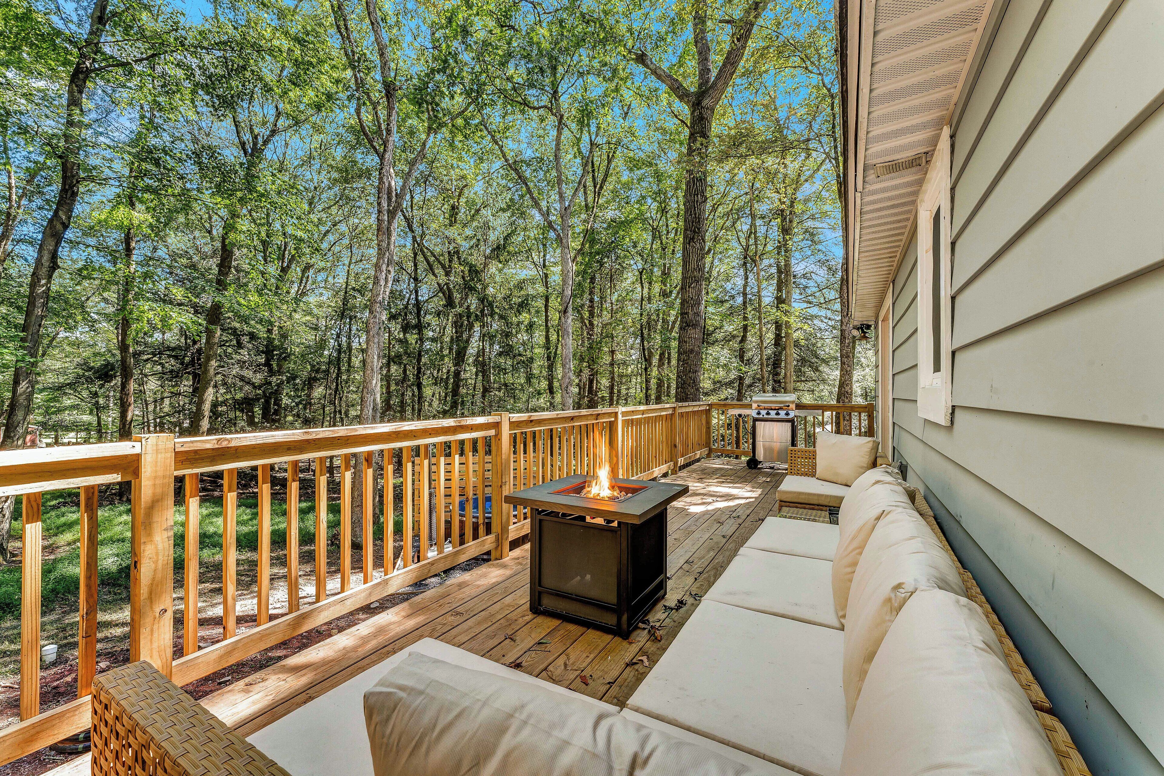 A deck with a fire pit, outdoor seating, and a view of a forest.