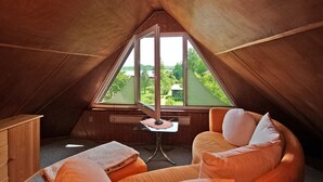 Een gezellig slaapkamer onder de dakpannen met een groot raam, een klein tafeltje en een comfortabele zithoek.
