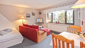 A cozy room with a red sofa, a wooden chair, a small table, a TV, and a window with curtains. - 1 bedroom awesome home in Malchow (Malchow)