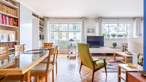 Un salon moderne avec un plancher en bois, un fauteuil vert, un téléviseur et des étagères remplies de livres.