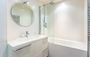 Un baño moderno con lavamanos, espejo y ducha blancos.