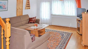 A living room with a sofa, a coffee table, a TV, and a bookshelf. - Ferienhaus Bärenstein (Bärenstein)