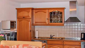 A kitchen with wooden cabinets, a microwave, a sink, and a stove. - Ferienhaus Bärenstein (Bärenstein)