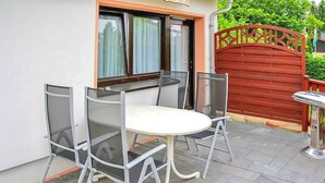 An outdoor patio with a round table and four chairs, a red gate, and a window with curtains. - Ferienhaus Bärenstein (Bärenstein)