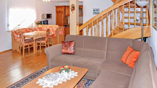 A cozy living room with a sofa, a dining table with chairs, a staircase, and a kitchen area. - Ferienhaus Bärenstein (Bärenstein)