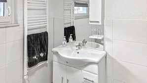 Ein Badezimmer mit einem weißen Waschbecken, einem Spiegel, einem Handtuchhalter und einem Fenster mit Blick auf ein Gebäude.