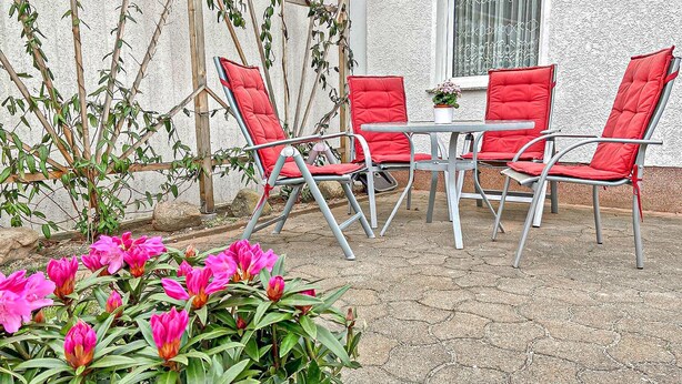 Eine Terrasse mit vier roten Sitzgelegenheiten und einem kleinen runden Tisch.