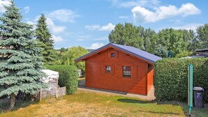 A wooden cabin with a sloped roof, surrounded by trees and a grassy yard.