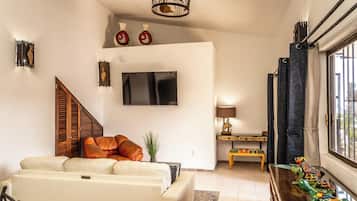 Una sala de estar con un sofá, un televisor montado en la pared, una escalera y una ventana con cortinas.