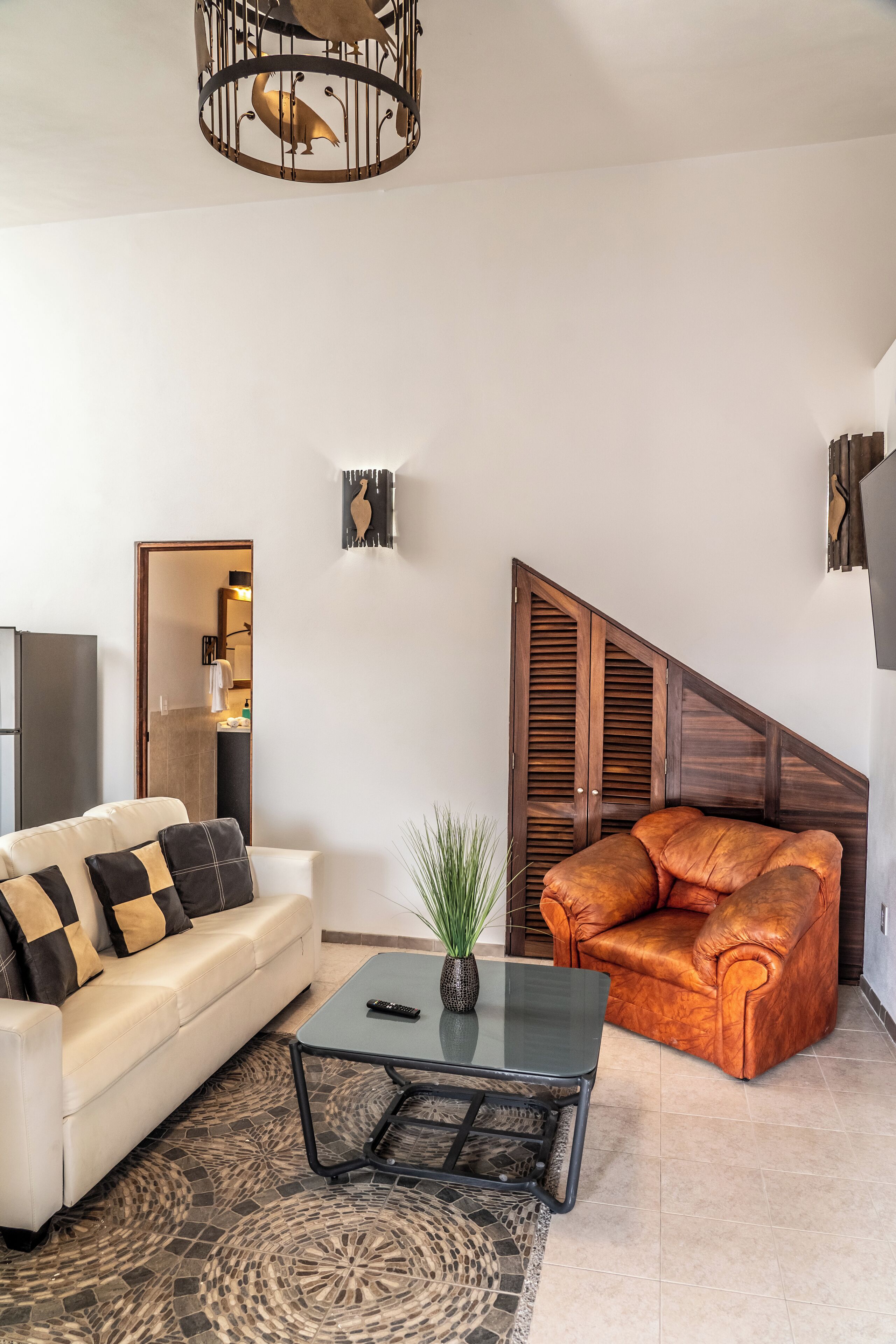 A living room with a white sofa, an orange leather chair, a coffee table, and a hanging light fixture.