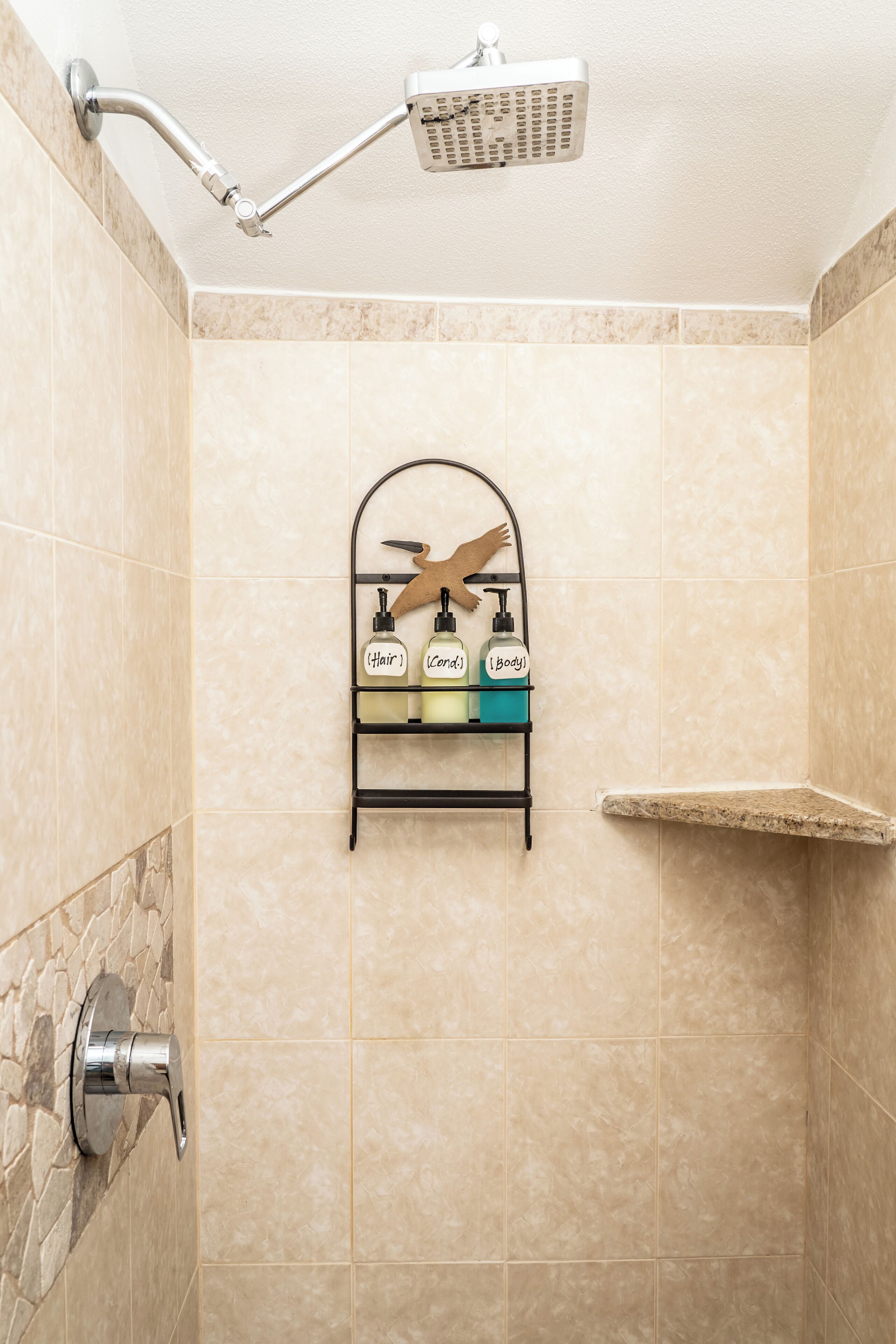A shower with a handheld showerhead, a wall-mounted shelf with toiletries, and a stone accent wall.