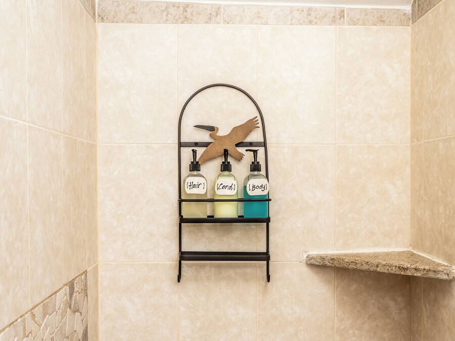 A shower with a handheld showerhead, a wall-mounted shelf with toiletries, and a stone accent wall.