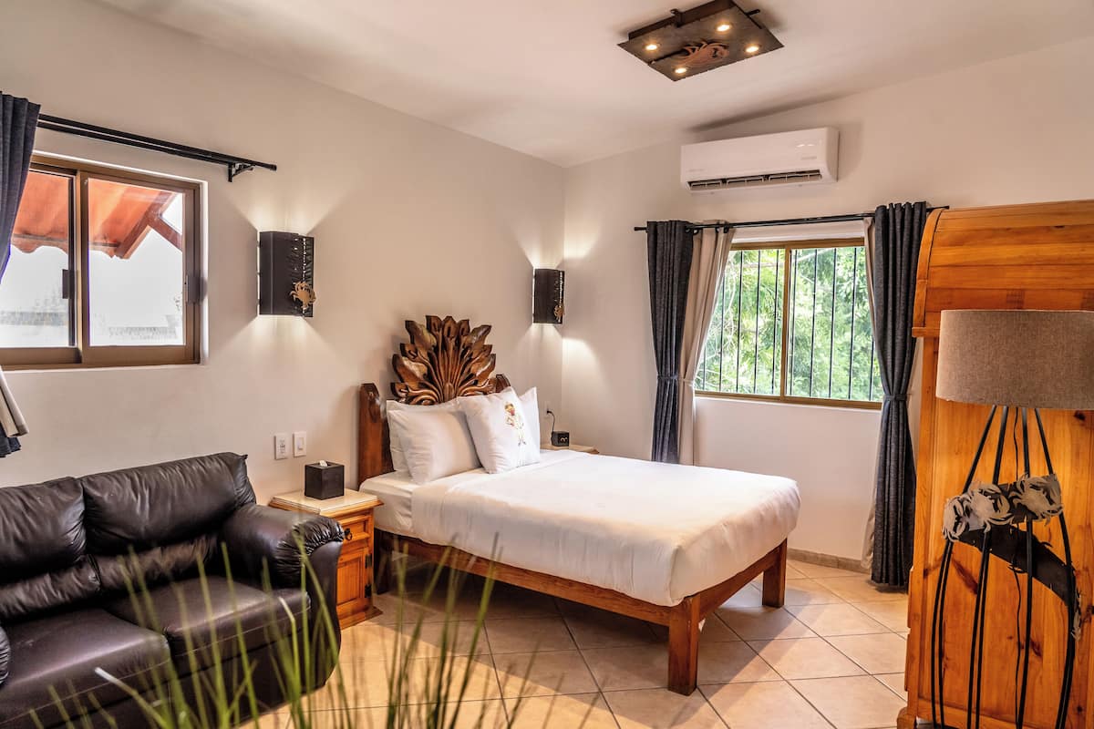 Ein Schlafzimmer mit einem Bett, einer schwarzen Ledersofa, einem hölzernen Kopfteil und einem Fenster mit Vorhängen.
