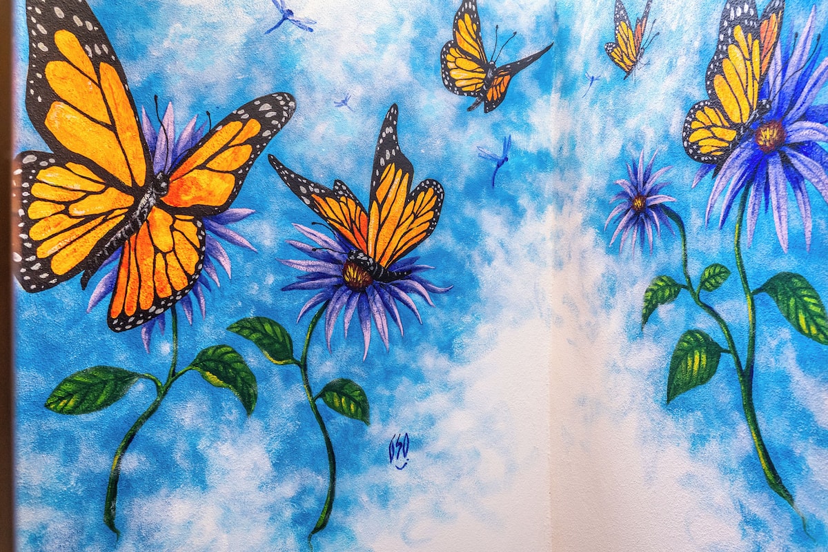 Ein Gemälde mit Schmetterlingen und Blumen vor blauem, strukturiertem Hintergrund.