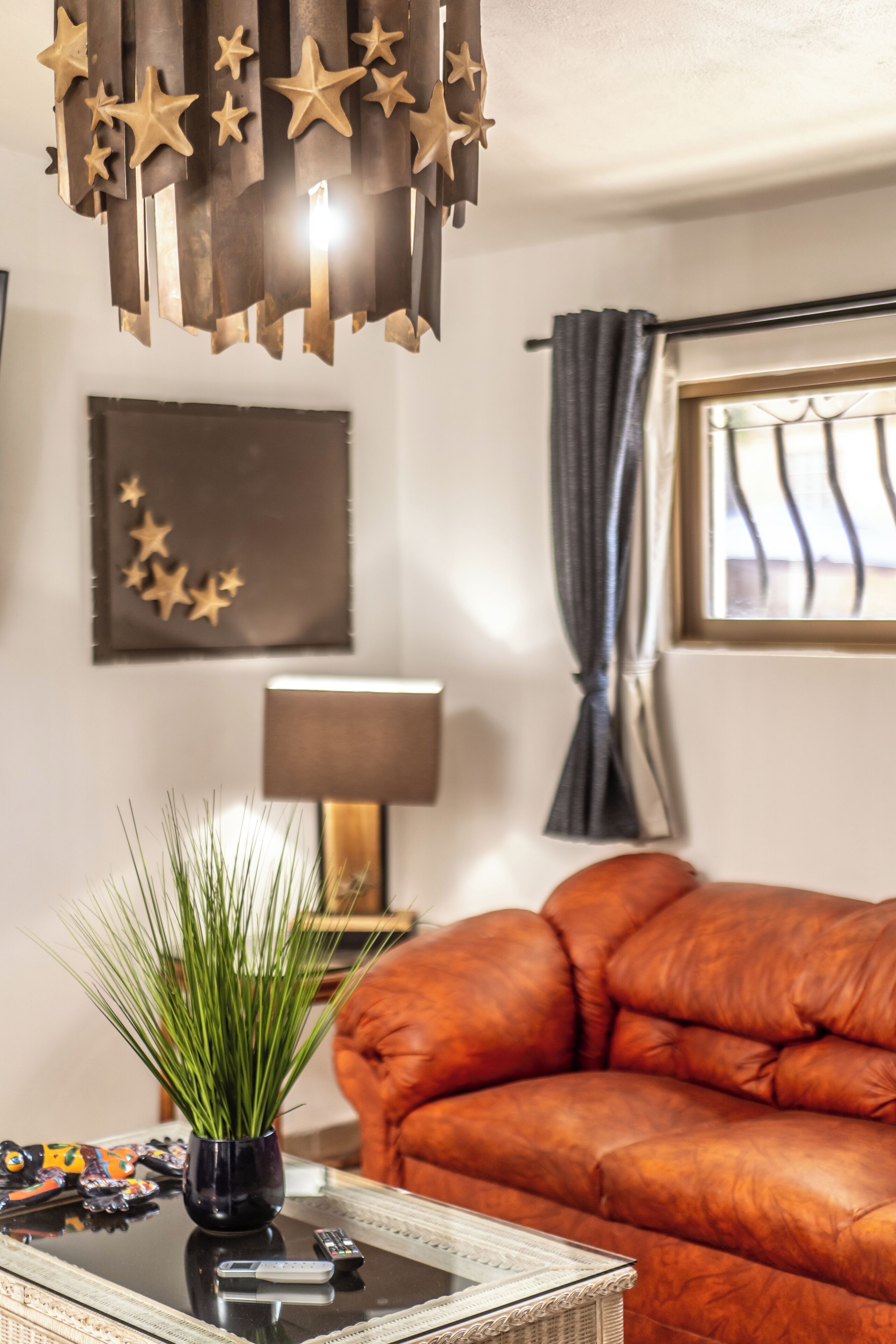 Ein Wohnzimmer mit einer Ledersofa, einem Glastisch mit Fernbedienung, einer Topfpflanze und einer sternförmigen Pendelleuchte.