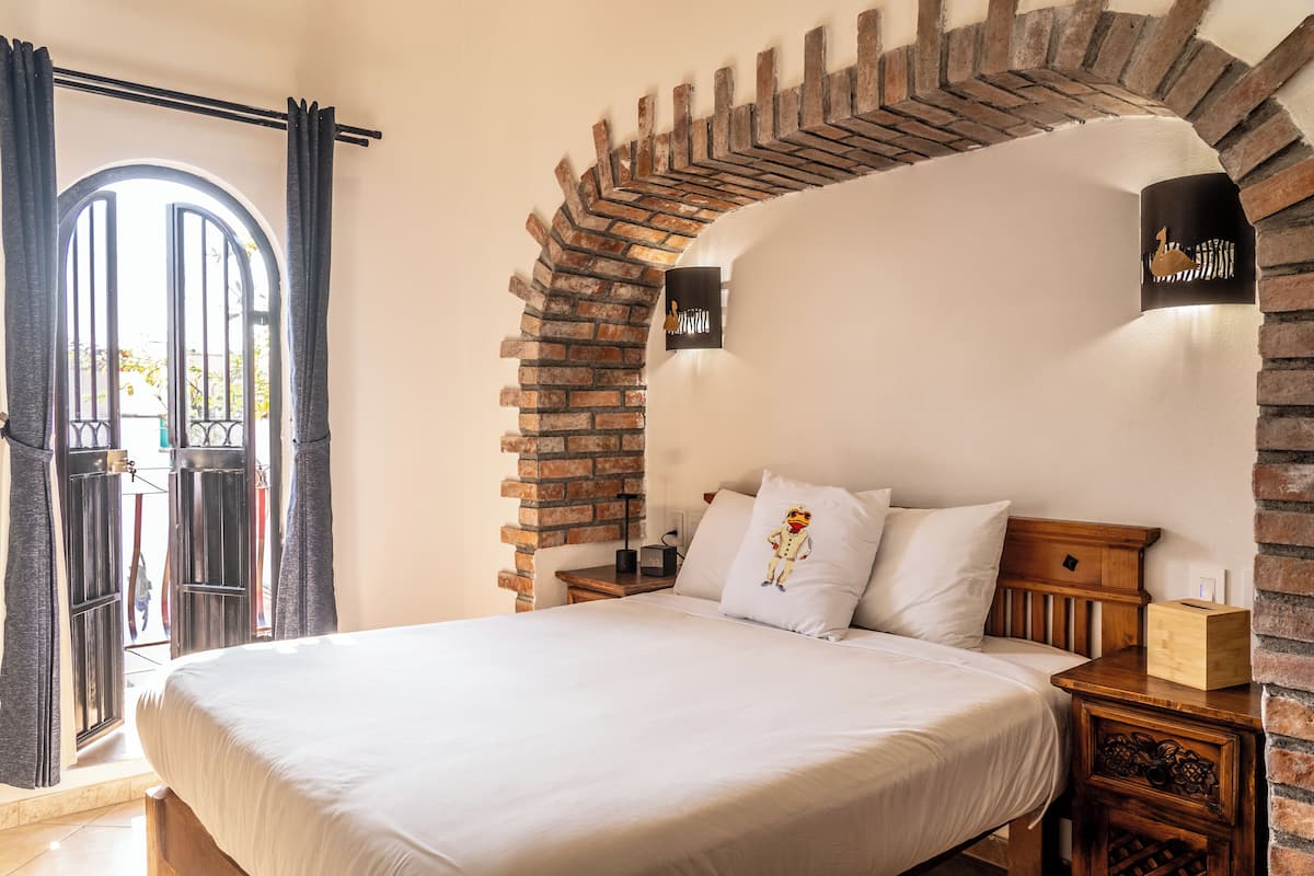 Ein Schlafzimmer mit einer Ziegelbogenarchitektur, einem Bett mit weißer Bettwäsche, einem Nachttisch und einer wandmontierten Leuchte.