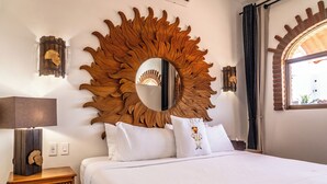 A neatly made bed with white linens, a large sun-shaped mirror above it, and a wooden nightstand with a lamp. - 5 Frogs Hotel Bucerias  (Bucerías)